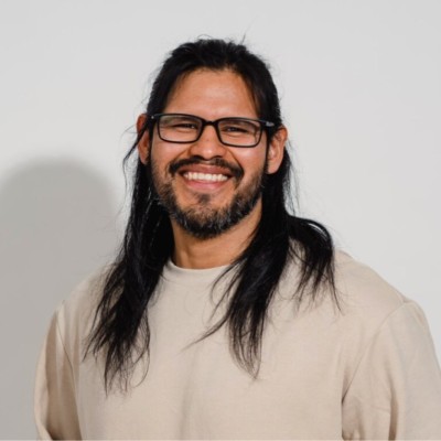 Portrait of Adair Campos smiling, wearing glasses and a light shirt.